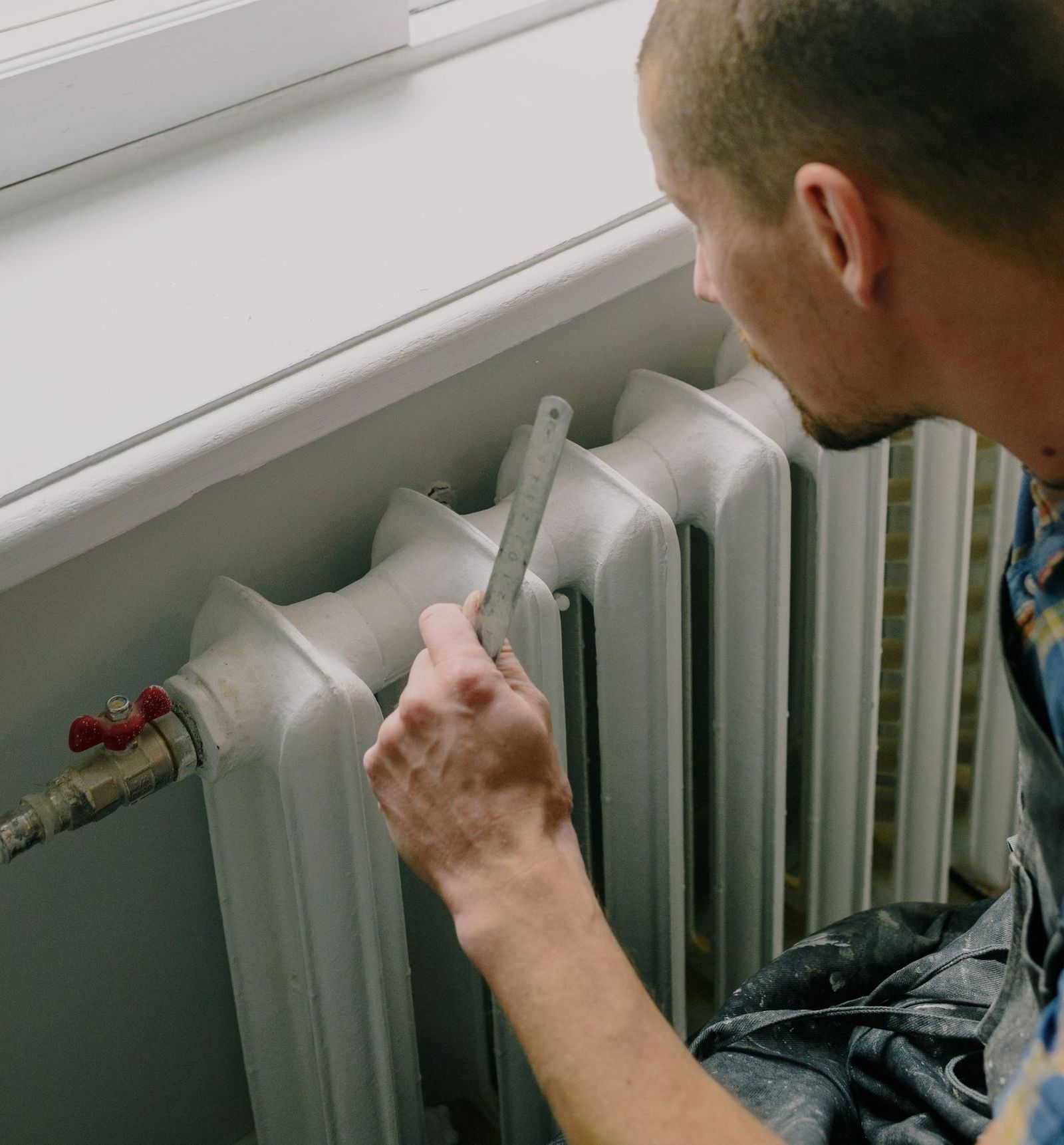 A heating engineer checking a radiator and its valve in a Surrey home